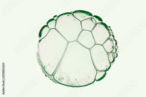 Macro shot of transparent cosmetic gel bubbles with green borders forming organic cellular structures on isolated white background.