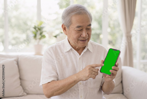 Elderly man smiling while pointing at smartphone with green screen