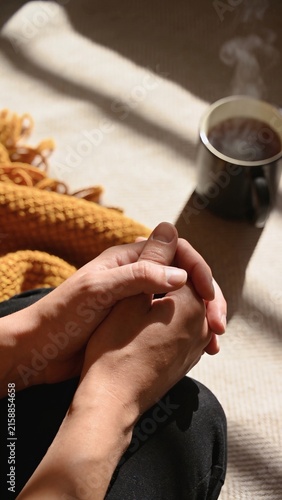 Close up of hands folded in prayer and meditation with steaming coffee mug vertical