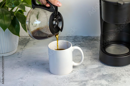 Принти на полотні Fresh brewed coffee being poured from a glass carafe into a white mug beside a drip coffee maker