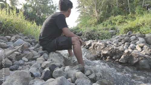 Man Sitting Beside a Flowing Stream in a Tropical Forest