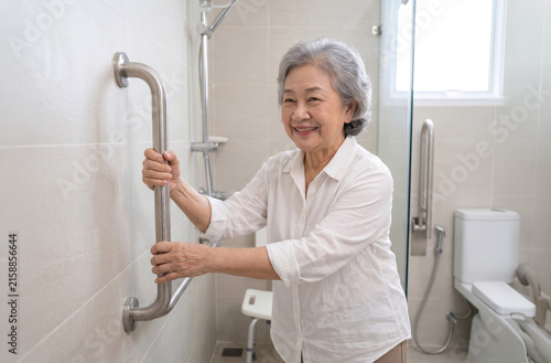 Elderly woman holding grab bar safety handrail in bathroom shower smiling