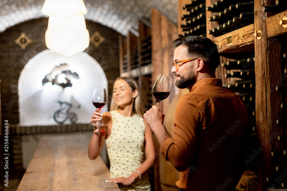 Naklejka premium Couple enjoys wine tasting in a cellar at a vineyard during an evening visit