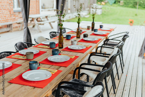 Konstfotografi Long wooden table arranged with white plates, ceramic mugs, red placemats, cutle