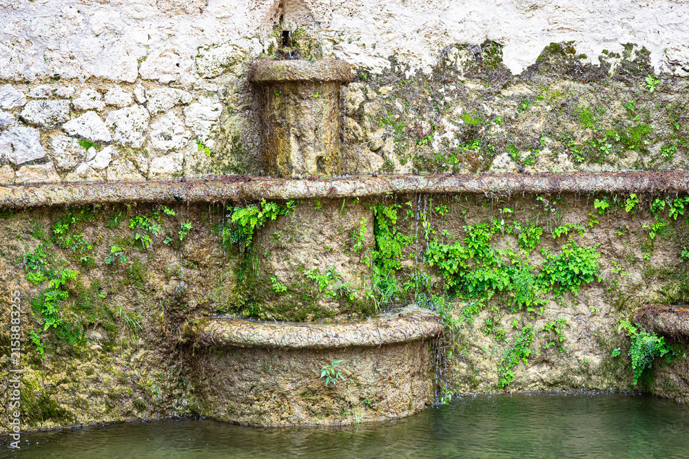 Fototapeta premium Old stone fountain against weathered wall in rustic courtyard