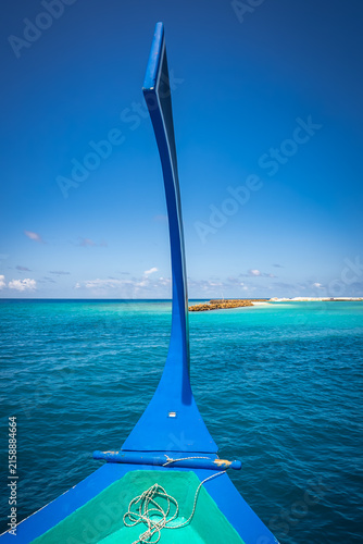 Foto The prow of a traditional wooden dhoni boat points toward a distant sandy atoll across vibrant turquoise waters under a sunny clear sky in Maldives