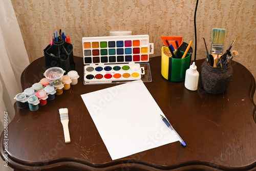 Art space includes a chair, chalkboard, easel, and plant in a room with plain walls and wooden floor