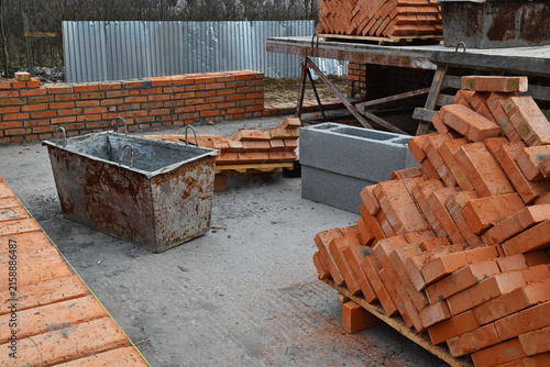 Obraz na płótnie An open-air construction site: stacks of red clay bricks, partially erected bric