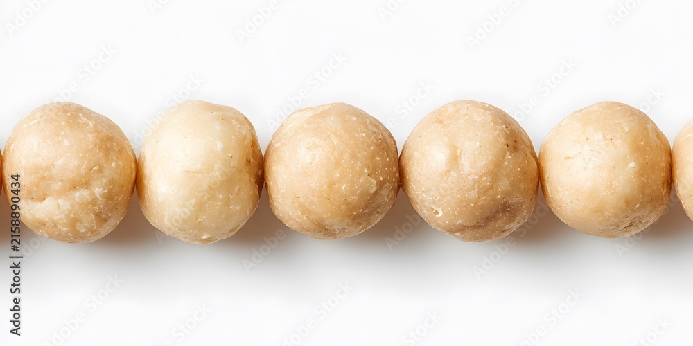 Fototapeta premium Several round macadamia nuts are arranged in a horizontal line against a white background.