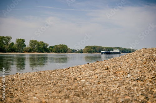 Extremes Niedrigwasser am Rhein mit freiliegendem Kiesufer und Frachtschiffen auf dem Fluss als Symbol für Dürre, Wasserknappheit und Probleme der Binnenschifffahrt.
