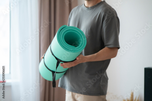 Someone holds a green yoga mat while entering a room with sunlight coming through the window