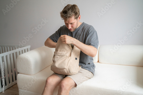 A man checks the contents of his backpack while sitting on a couch in a home setting