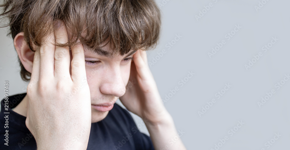 Fototapeta premium Young man suffering from a painful headache or migraine, holding his temples with both hands, conveying stress, mental fatigue, and a health problem