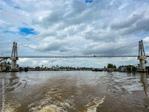 фотографія Wide suspension bridge spans murky river under cloudy sky