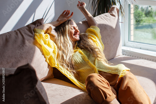 Konstfotografi Happy woman relaxing on a sofa in bright sunlight at home