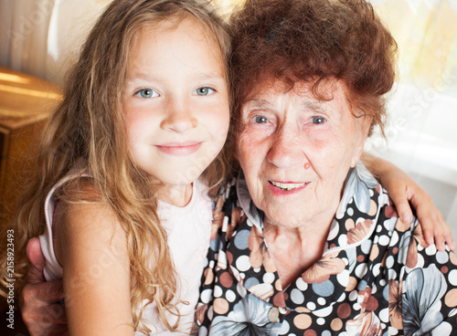 Canvastavla Smiling grandmother embracing her young granddaughter at home