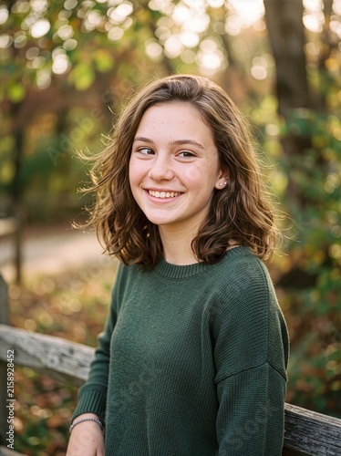 A smiling photograph of a young girl with a slight squint in one eye, taken in the forest.