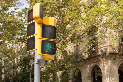 Green Pedestrian Signal On Yellow Traffic Light At Urban Crosswalk With Historic Building Background