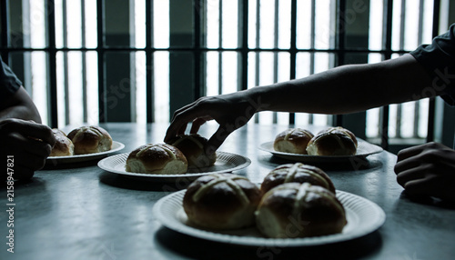 Prison cafeteria table with shared hot cross buns on paper plates. Silhouetted hands