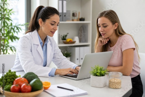 Professional female doctor discussing healthy nutrition with young client using laptop in bright modern kitchen with fresh produce