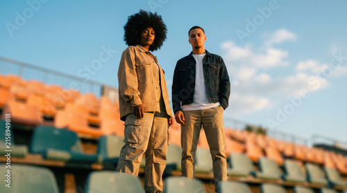 Two young adults standing confidently in stadium seating under warm golden hour light