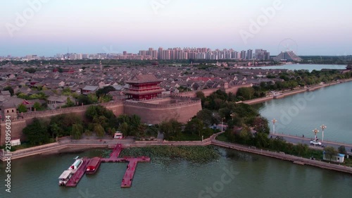 A panoramic view of an ancient city with well-preserved city walls, traditional architecture, and adjacent water bodies, with modern urban skyline in the distance.