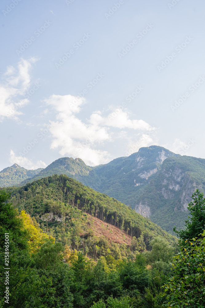 Fototapeta premium scenic green mountain landscape with forested hills under blue sky and scattered clouds