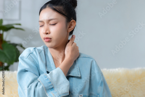 woman suffering from neck pain and stiffness while holding her neck at home, representing muscle tension, discomfort, fatigue, poor posture, stress and everyday wellness concerns.