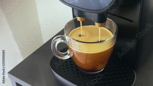 Coffee machine pouring hot espresso into a transparent glass mug, creating a creamy foam for a delicious and invigorating morning caffeine boost with a rich aroma