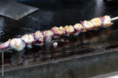 Foto Grilled octopus skewer on hot metal grill with charred edges and glistening oil,