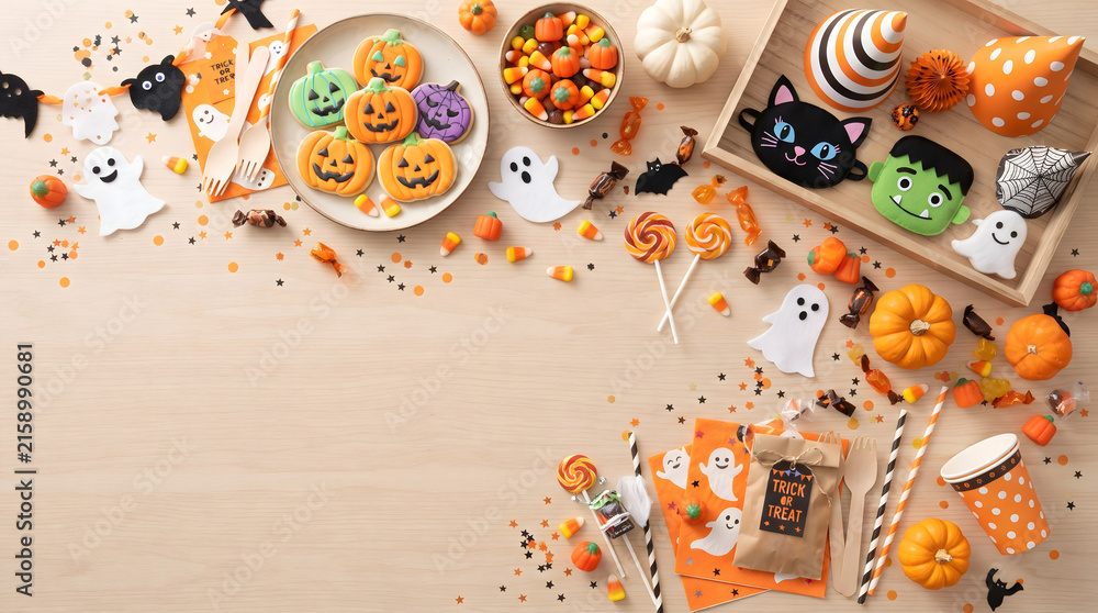 Fototapeta premium Creative Halloween flat lay background with festive cookies, candies, cute decorations, and small pumpkins on a wooden table