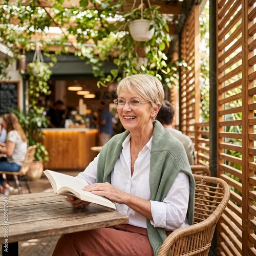 Smiling senior woman reading a book in a lush outdoor café