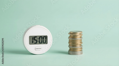 Time is money concept with a digital timer displaying fifteen minutes next to a stack of coins