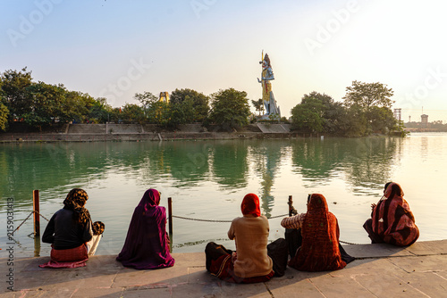 India. Uttarakhand. Haridwar. A group of Indian women are resting in front of the monumental statue of the god Shiva on the banks of the Ganges at sunset