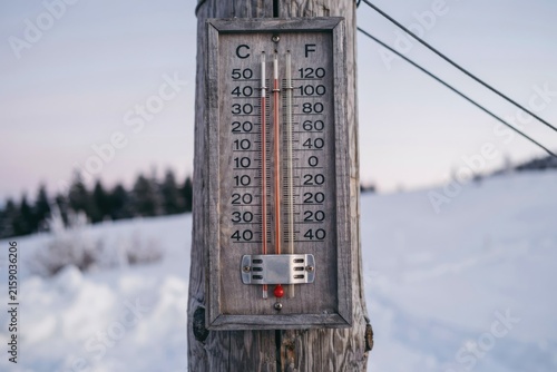A vintage outdoor thermometer attached to a wooden post indicates freezing temperatures in a snowy winter landscape. Ideal for climate or weather reports.