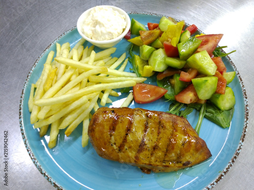 Grilled chicken breast and French fries with a fresh vegetable salad. Delicious and healthy for lunch or dinner. Healthy eating. Cucumbers, tomatoes, bell peppers, and sauce.