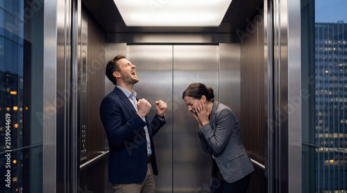 Excited business founders celebrating success silently inside a modern office elevator