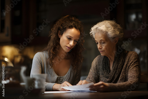 Adult daughter helps elderly mother with paperwork at kitchen table
