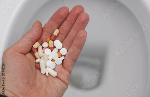 Fotografie Hand holding a lot of pills against the background of a toilet