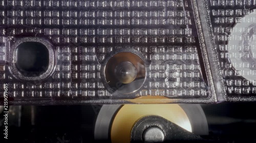 Metal capstan spindle and pinch roller rotating to pull magnetic tape ribbon of retro audio cassette tape. Detailed macro shot