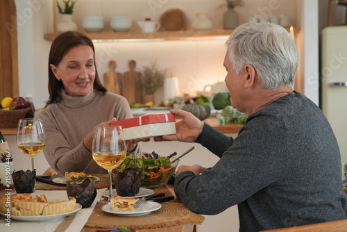 The elderly couple smiled happily. The grandfather held a gift box for the grandmother, who was surprised and delighted to receive the gifts as they celebrated Christmas and New Year with their family