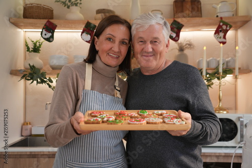An elderly couple, smiling happily, dressed in aprons, carried wooden trays and baked and decorated gingerbread cookies together to celebrate Christmas with their family.