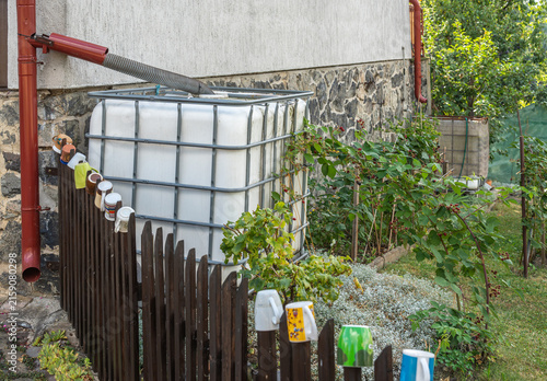 Large rainwater harvesting storage tank installed on house downspout, saving water for sustainable garden irrigation