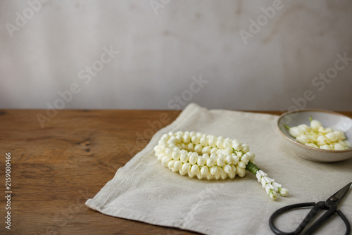 Sampaguita bud garland with scissors and ceramic dish on linen cloth, floral craft and handmade workspace theme