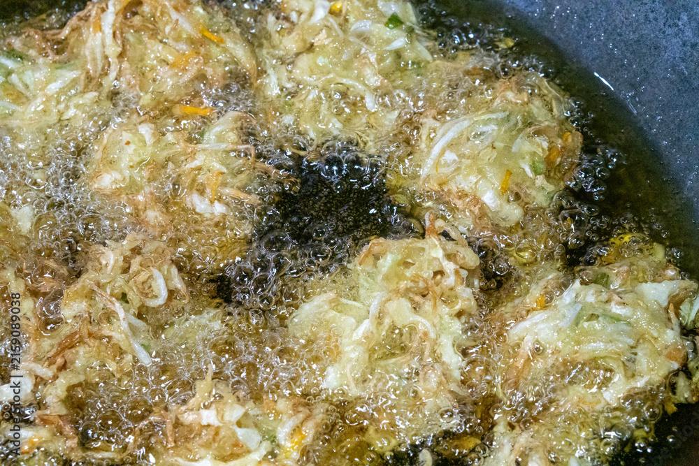 Fototapeta premium Vegetable fritters frying in hot oil in a wok. The main ingredients consist of sliced ​​cabbage, sliced ​​carrots, and sometimes bean sprouts