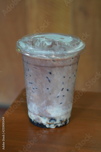 front view iced chocolate and cocoa drink in a clear plastic cup, on wooden floor, brown wooden wall background, drink, cool, copy space
