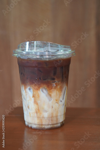 front view iced coffee and caramel Macchiato drink in a clear plastic cup, on wooden floor, brown wooden wall background, drink, cool, copy space