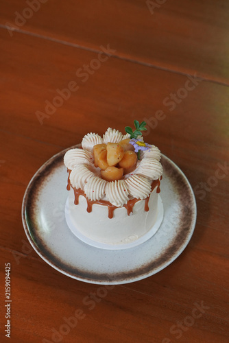 top view sweet macadamia caramel and coffee cake and decorated with purple and yellow flowers, whipped cream, and macadamia nuts on brown and white ceramic plate on wooden floor background