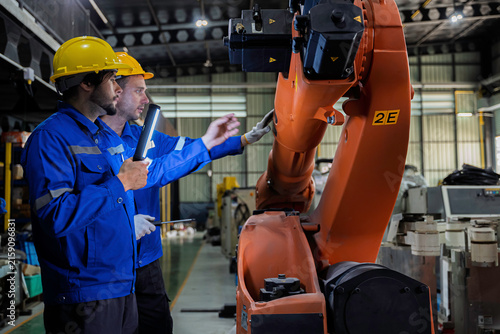 Two industrial engineers inspect a robotic arm during maintenance in a smart manufacturing facility, highlighting automation, engineering, teamwork, industrial robotics, and advanced production 