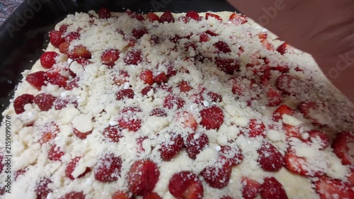 Close-up of hand sprinkling sweet crumble topping over fresh strawberry sheet cake